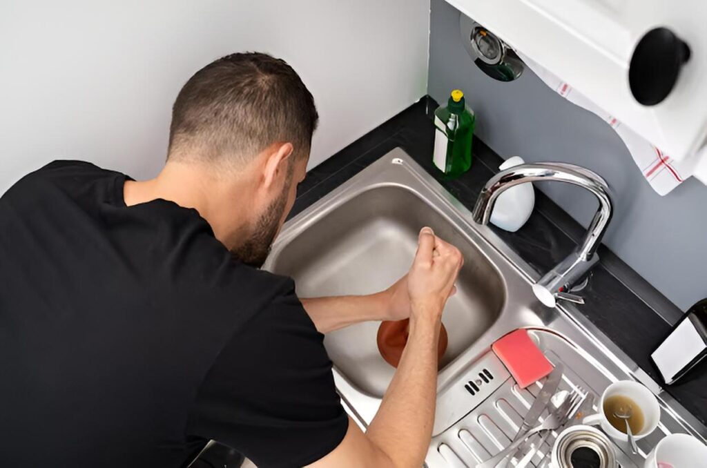 person using a plunger to unclog kitchen sink