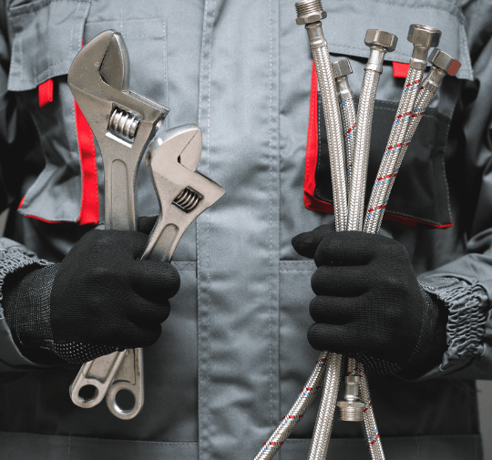 Pipe relining Sydney expert in gray uniform and gloves holding adjustable wrenches and flexible metal hoses.