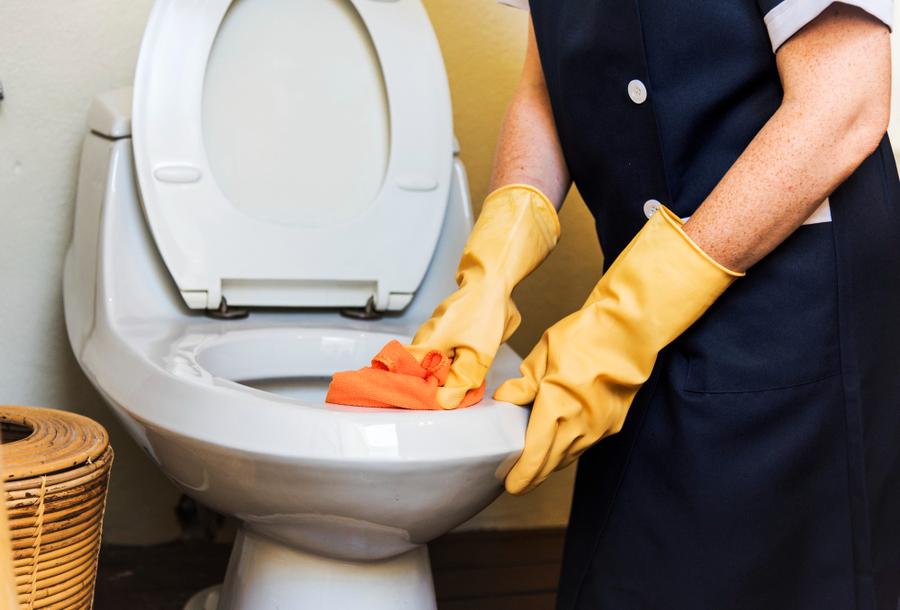 A person in yellow gloves cleans a toilet with an orange cloth, keeping the bathroom spotless for Sydney toilet repairs.