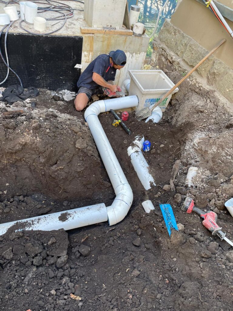 A worker in a cap installs white PVC pipes in a trench with tools Plumber Paddington at work onsite.