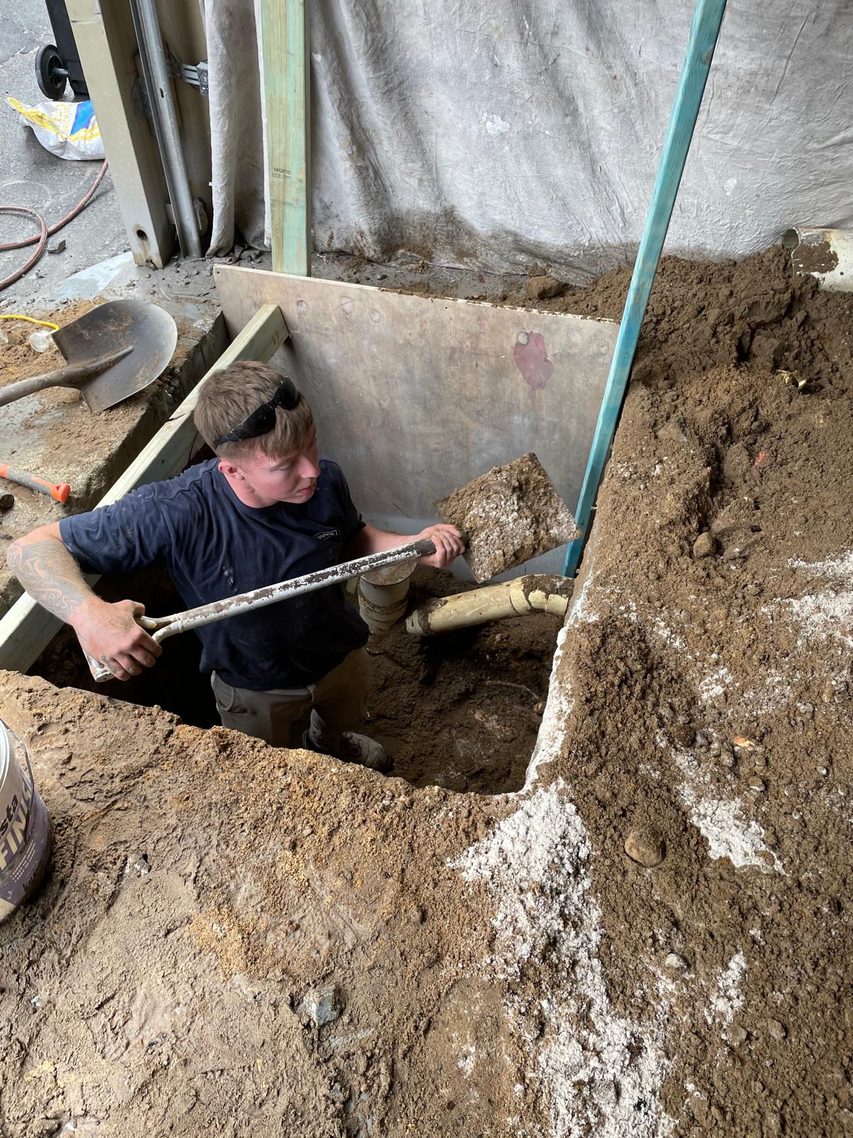 Plumber in Vaucluse installs or repairs pipe in trench near building, using level—Vaucluse Drainage Challenge.
